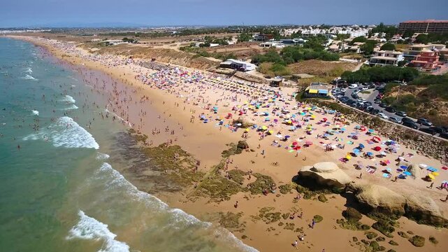 Aerial view of crowded gale beach in albufeira, algarve, portugal, with numerous tourists sunbathing under colorful umbrellas and swimming in the atlantic ocean on a sunny summer day