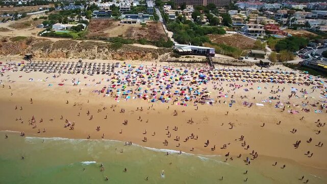 Aerial view flying over crowded sandy beach with colorful umbrellas and tourists swimming in ocean on sunny summer day in albufeira, algarve, portugal, popular travel destination. Gale Beach