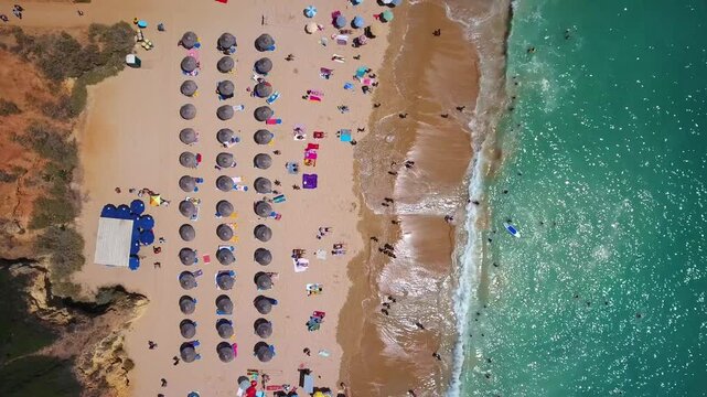 Stunning top down aerial view of a crowded sandy beach with colorful umbrellas and people swimming in the turquoise ocean, a perfect summer vacation scene with gentle waves washing ashore