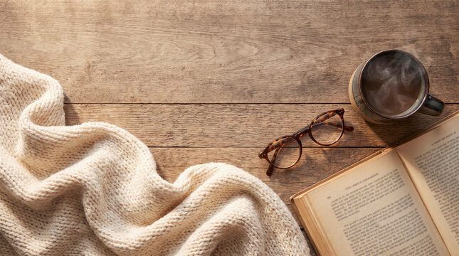 Flat lay of chunky knit blanket, glasses and book with steaming coffee
