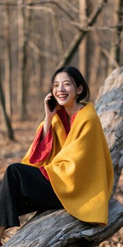 Smiling woman wrapped in a yellow shawl talking on a phone in a bare forest for lifestyle and communication banner