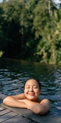 Fototapeta premium Woman smiling in pool at the edge with tropical trees in background for spa relaxation background and wellness poster design