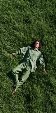 Top view of a woman lying on tall green grass in a matching outfit for lifestyle wellness background and banner design