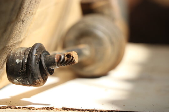 Close up of an old vehicle steering mechanism resting on a wooden surface. Tie rod end from automobile part