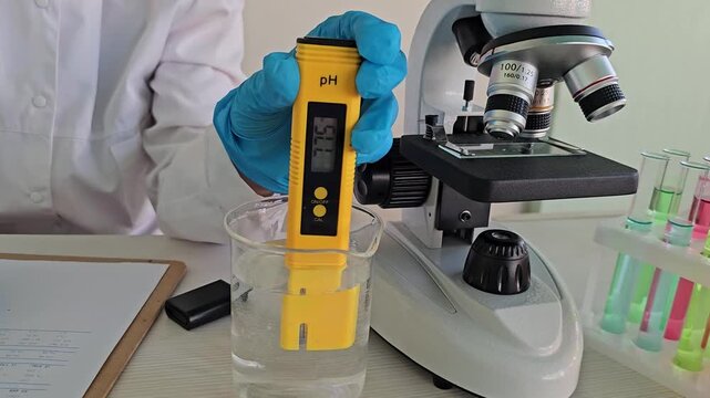 Testing pH levels with a meter at a lab table using a microscope and glass containers