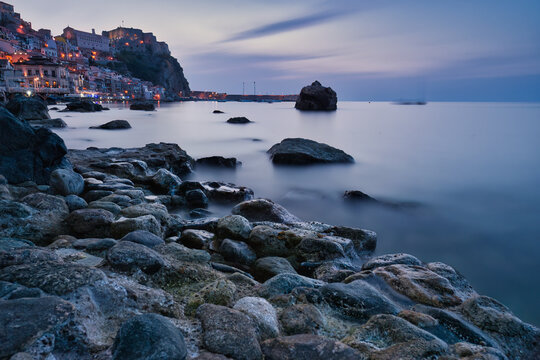 Long exposure blue hour view of Chianalea village and Ruffo Castle from the rocky shore, Scilla, Calabria, Italy