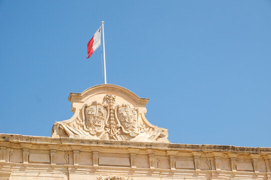 Ornate stone pediment with Maltese flag against blue sky