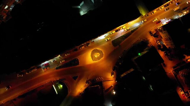 Bird's eye view of illuminated roundabout with moving cars, night