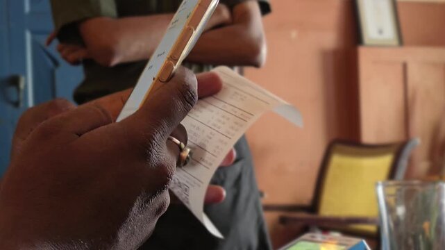 Making a digital UPI payment using a smartphone application while a waiter stands with folded arms waiting for the final mobile bill transaction confirmation inside a restaurant.