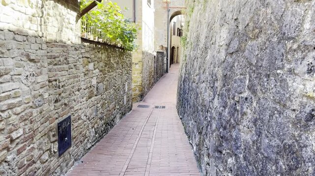 Narrow brick alleyway between ancient stone walls in an Italian town, historic street, travel destination.