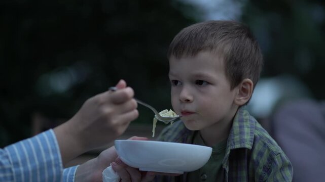 Mother carefully feeds her young son soup from a bowl with a spoon in a restaurant. Authentic family moment of parenting, love, care and bonding over a meal.