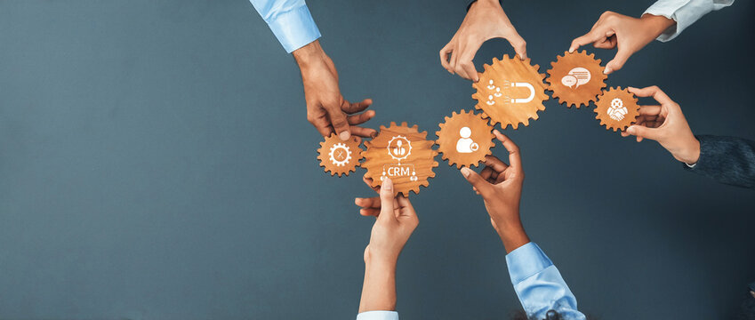 Diverse hands collaborate over gears showcasing icons related to customer relationship management, emphasizing teamwork for innovative business strategies and effective solutions. Amity