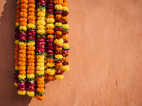 Marigold and rose flower garlands hanging on orange wall