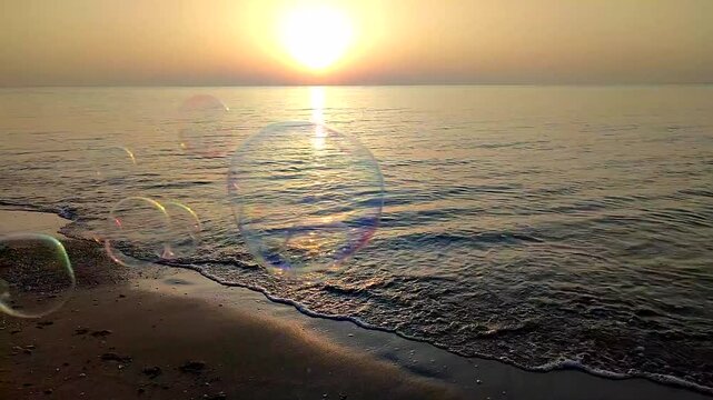 Flying soap bubbles on background of the sea during dawn sunset. Lots of soap bubbles against background of calm sea and sandy beach on dawning sundown. Romantic cheerful fun nature natural backdrop