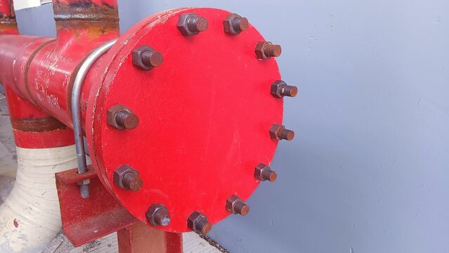r Close-up of a red industrial pipe flange with multiple bolted fasteners, steel piping, and mechanical connections used in industrial infrastructure and fluid transfer systems.