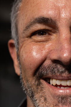 Senior man smiling, showing graying stubble beard and teeth, wearing dark collared shirt in studio