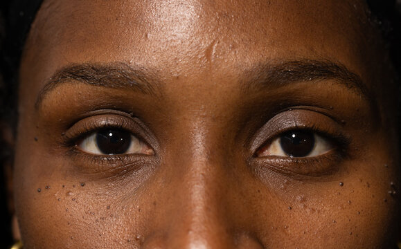 Woman gazing steadily into camera in studio, showing skin texture, small bumps, gold earring