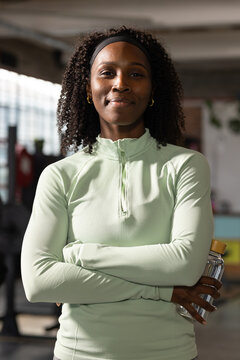 Mid adult woman standing in gym holding clear bottle with gold-lid wearing mint top, black headband