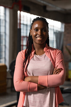 African American woman standing arms crossed in loft studio wearing coral jacket near grid windows