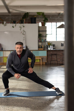 Middle-aged man performing lateral lunge on blue mat in loft studio wearing gray sneakers