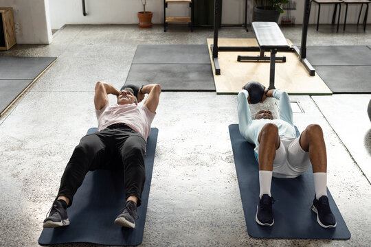 Two men lying on exercise mats holding medicine balls and doing core exercise in gym studio