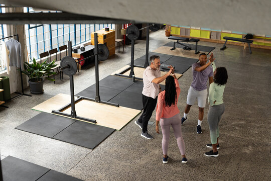 Diverse workout group in sportswear high-fiving in gym near squat racks and barbells, copy space