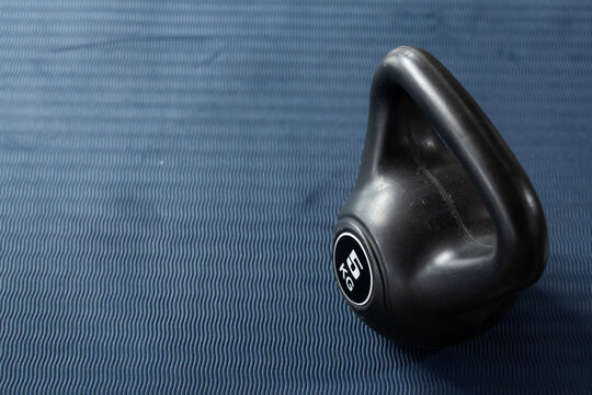 Black kettlebell is resting on blue textured exercise mat at right, showing 16 KG label
