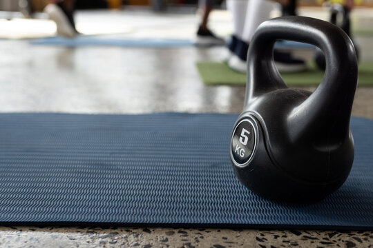 Black kettlebell labeled 5 KG is resting on blue textured mat on polished concrete floor
