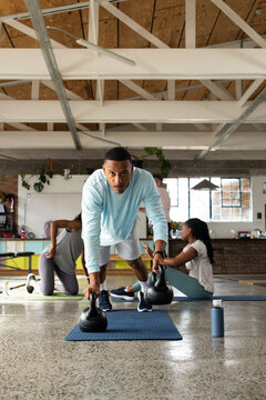 Diverse workout group with African American instructor holding plank on kettlebells at loft studio
