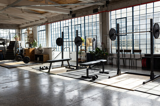 Three squat racks and benches are sitting on wood platforms in loft gym, light casting shadows