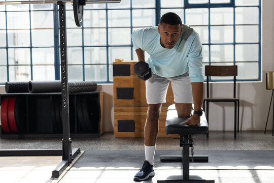 Man in blue top performing bent-over row on bench at gym on mat, pulling hex dumbbell