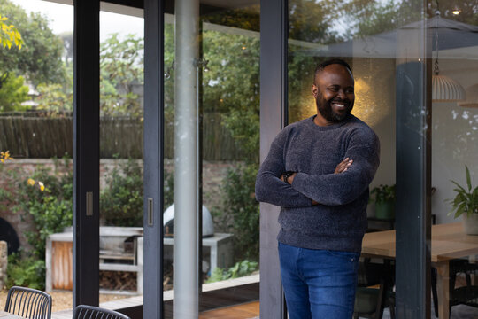Adult African American man standing leaning by glass doors at home, smartwatch showing, copy space