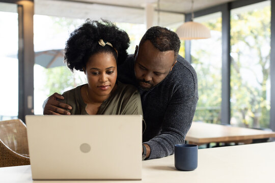 Couple leaning and working on silver laptop at home table with navy mug wearing casual sweaters