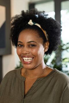 African woman smiling and posing at home with headband, olive-green blouse, plants