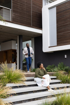 African couple sitting on concrete front steps, woman in olive sweater, man holding mugs