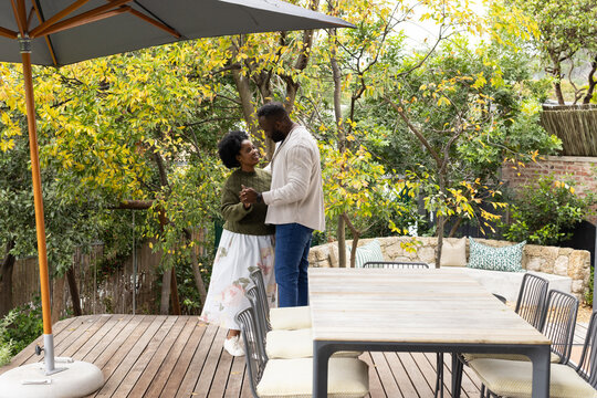African couple dancing slowly on wooden backyard deck near dining table woman in green sweater