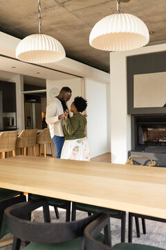 African American couple dancing, holding hands in kitchen by table, lamps overhead in casual attire