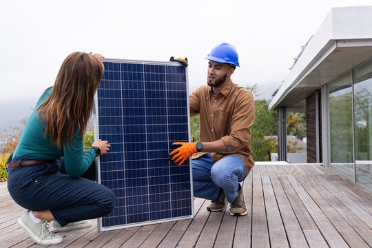 African American team kneeling on deck near sliding door wearing blue helmet installing solar panel