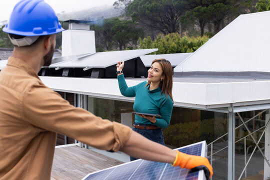 African American tech and owner pointing with tablet while tech handling panels with helmet on roof