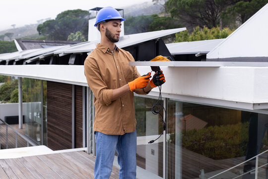 Man wearing blue hard hat and orange gloves using power tool on modern roof terrace