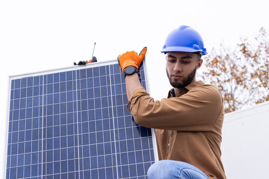 African American male tech placing solar panel on roof with blue helmet, orange gloves, copy space