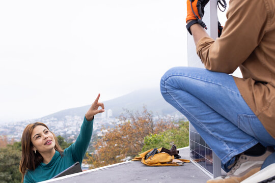 African American coworkers installing solar panel on flat roof, woman holding tablet, copy space