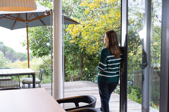 African American woman standing at sliding glass door wearing green striped sweater, copy space