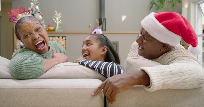 Senior couple and youth granddaughter laughing on couch as reindeer headband lighting for Christmas