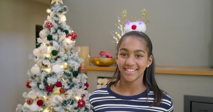 African American teen reacting to prompts smiling at home wearing antler headband by Christmas tree