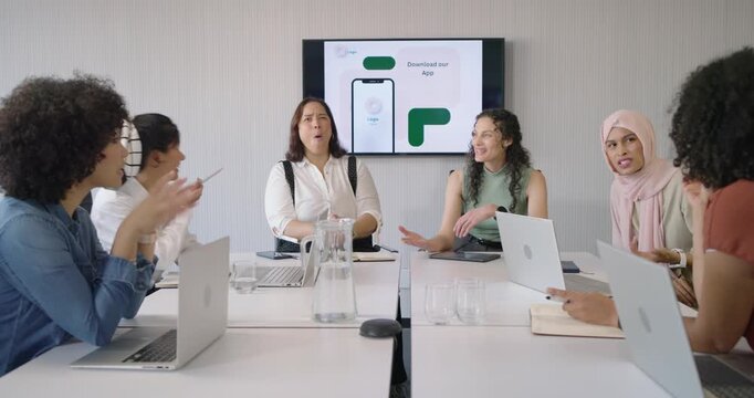 Diverse female team in work attire watching wall monitor showing app mockup, reacting, taking notes