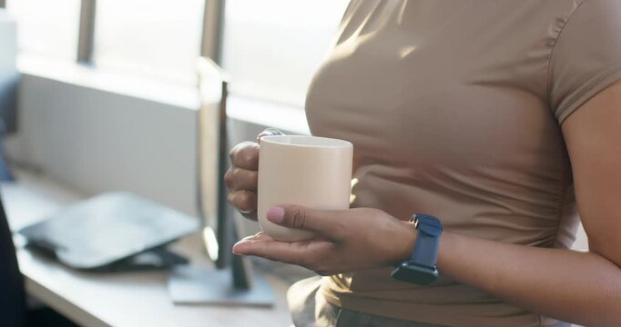 After grabbing ceramic mug, woman is holding and adjusting grip while taking desk break by window