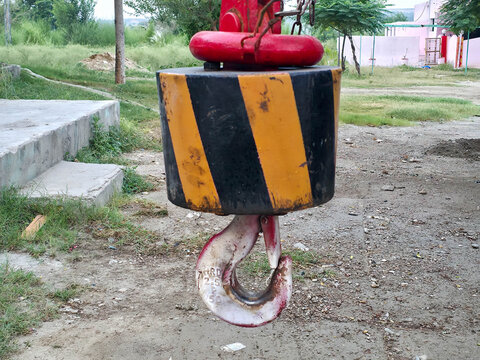 Heavy duty crane hook with yellow and black warning stripes for industrial construction site.