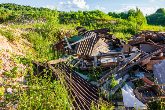Discarded construction debris and scrap materials piled in a disused quarry site, abandoned junk littering the overgrown landscape with metal sheets, weathered wood, and garbage waste