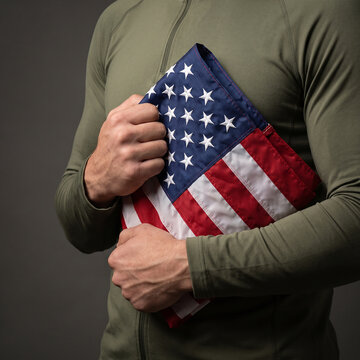 Man in military green clothing holding folded american flag closely.
